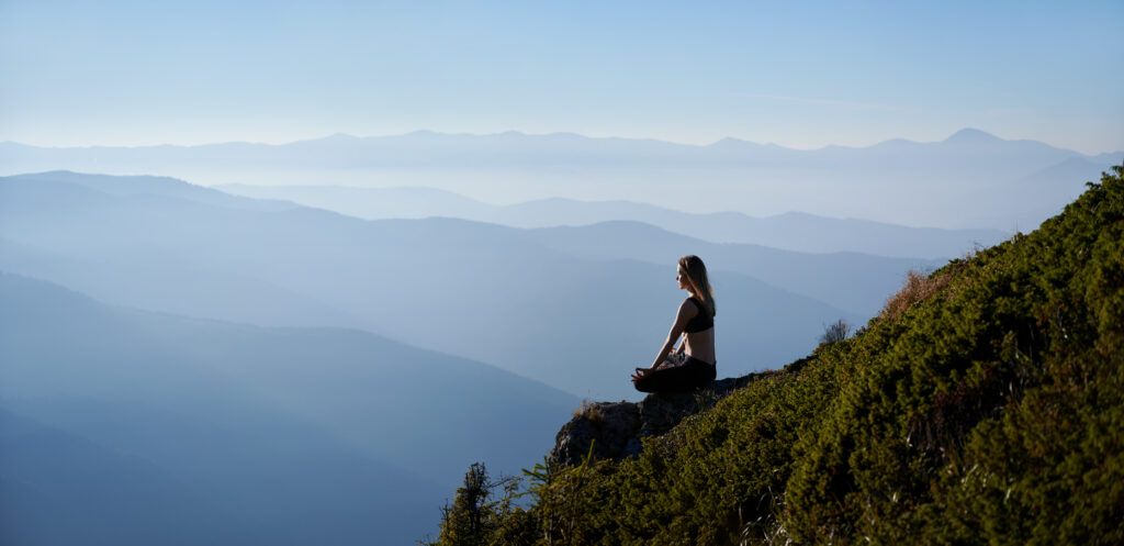 bienfaits montagne santé : jeune femme qui médite face à la montagne